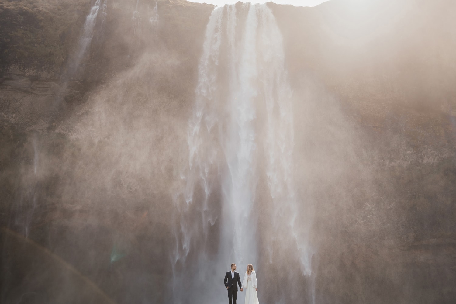 Bride and groom holding hands in front of Seljalandsfoss waterfall