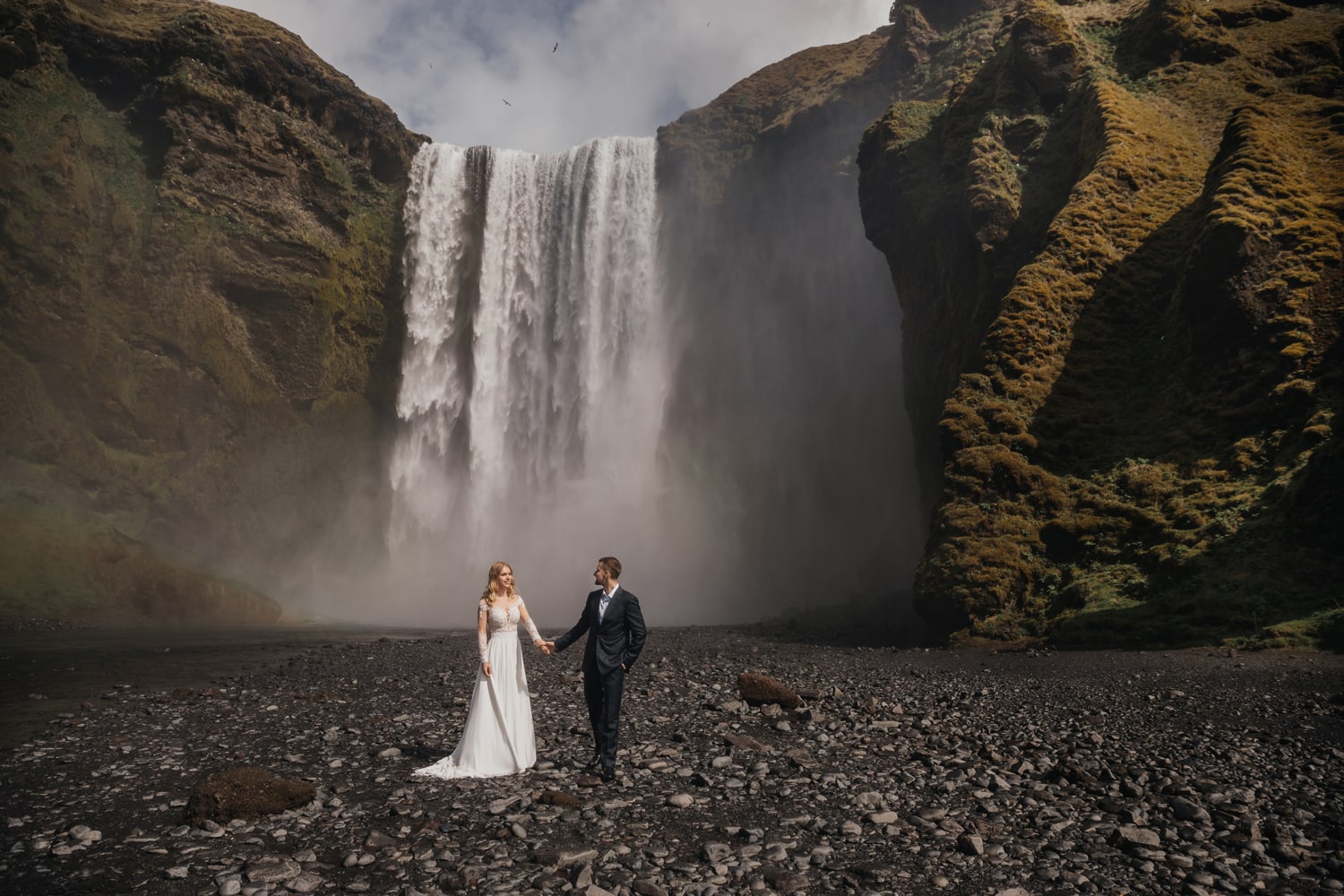 Bride and groom posing in front of Skógafoss waterfall