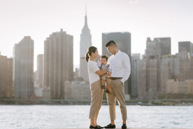 Family of three is posing at Gantry Plaza State Park with the midtown Manhattan skyline in the background