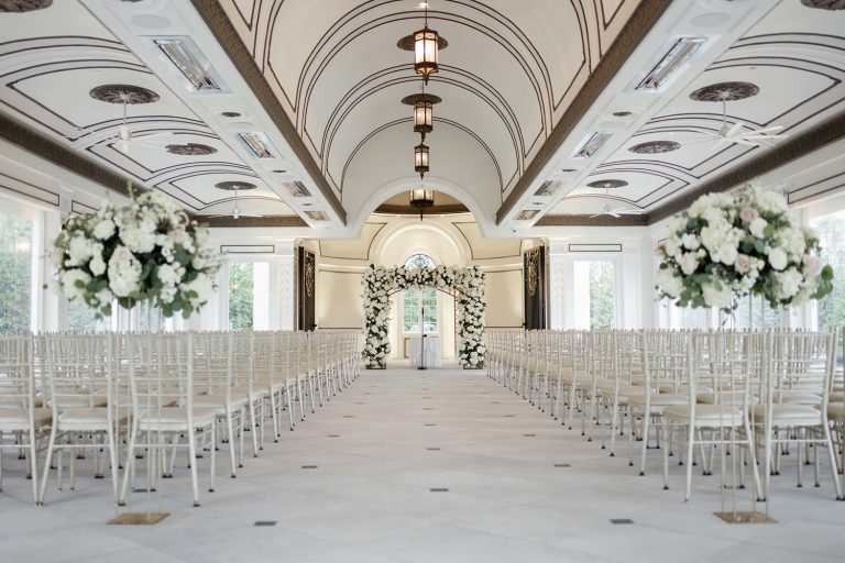 a beautifully decorated wedding ceremony setting at Shadowbrook at Shrewsbury Pavilion, featuring elegant chairs arranged in rows and a green floral arch