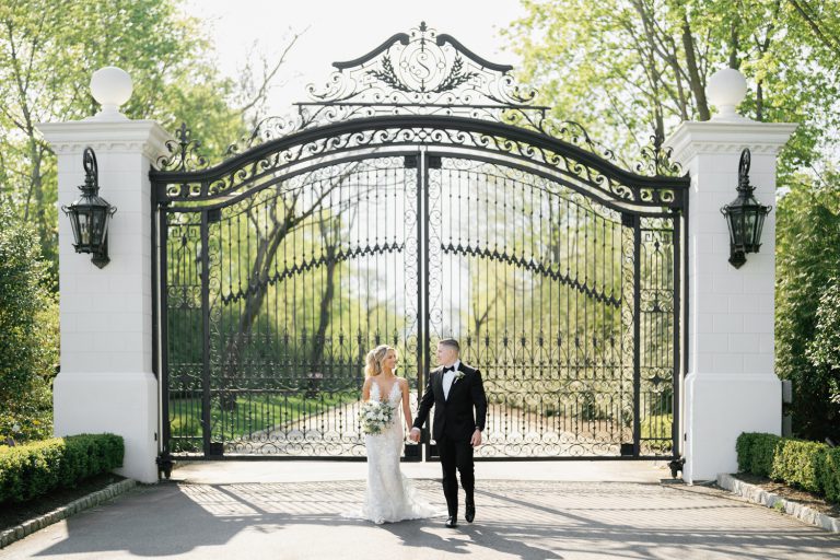 A romantic photo of a wedding couple standing hand in hand in front of the gates of Shadowbrook at Shrewsbury, exuding love and happiness on their special day.