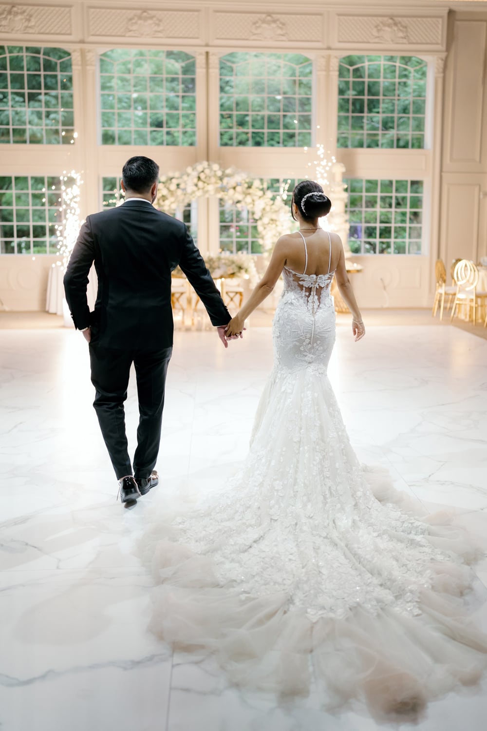 A happy bride and groom walk hand in hand through the elegant Grand Ballroom at the picturesque estate of Florentine Gardens in New Jersey, radiating joy and love on their special day.