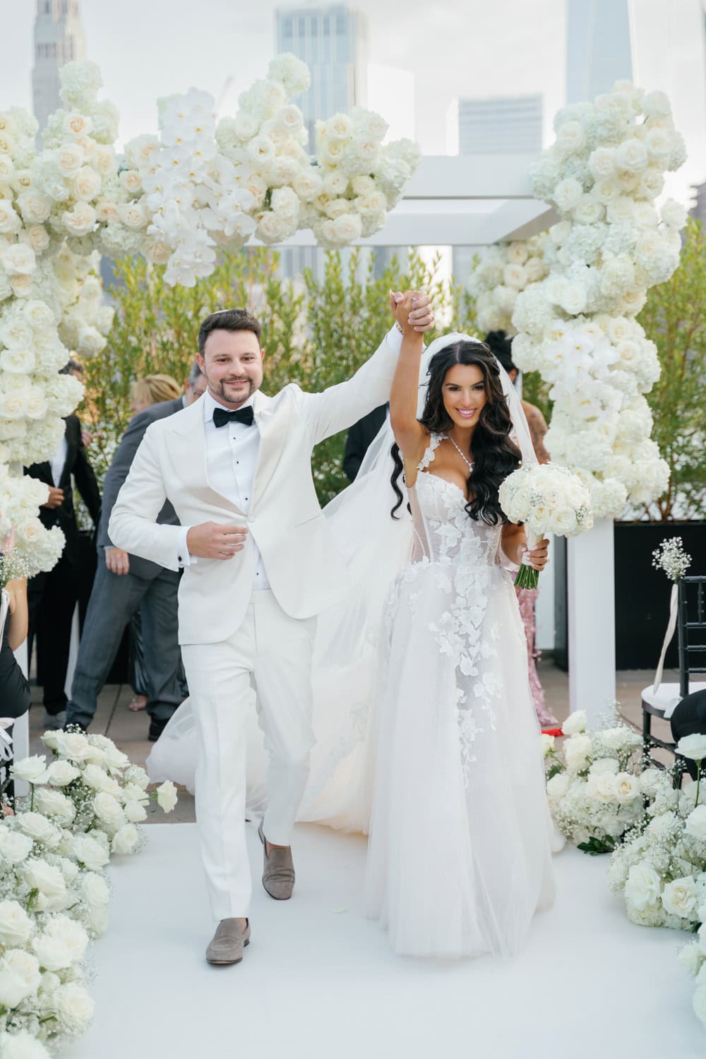 Newlywed couple celebrating their rooftop wedding ceremony with a stunning floral arch and NYC skyline at Tribeca Rooftop.