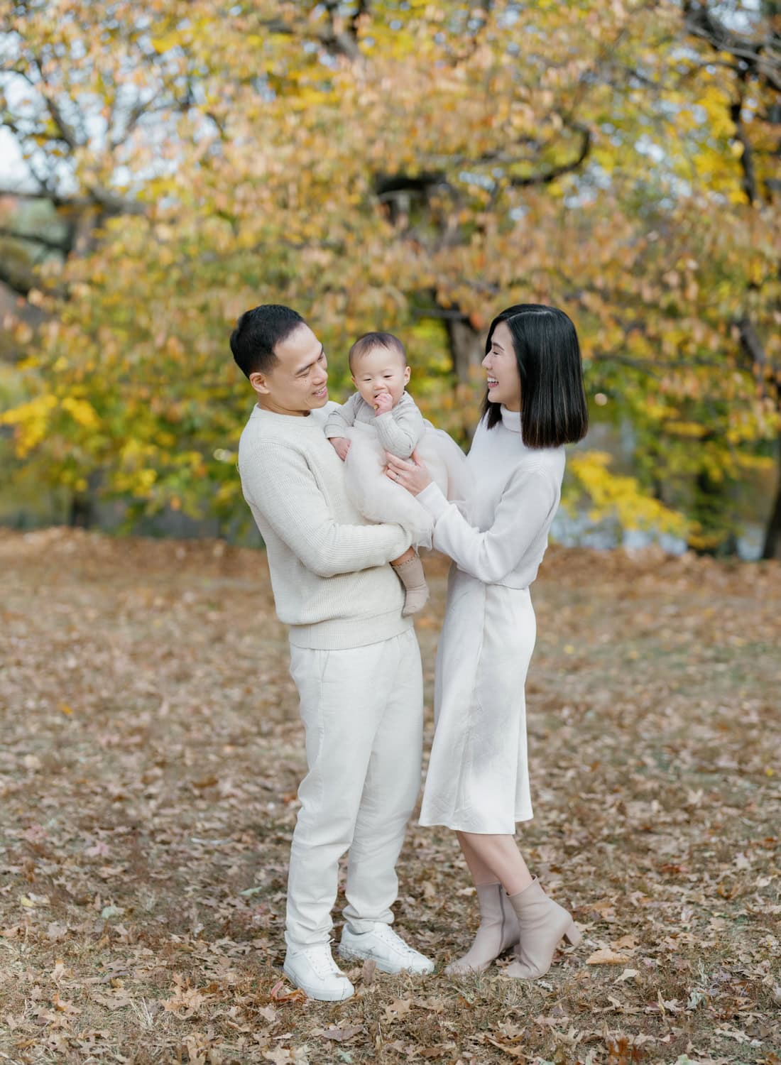 A joyful family dressed in neutral tones during a fall family photo session in Westchester, surrounded by golden autumn leaves.