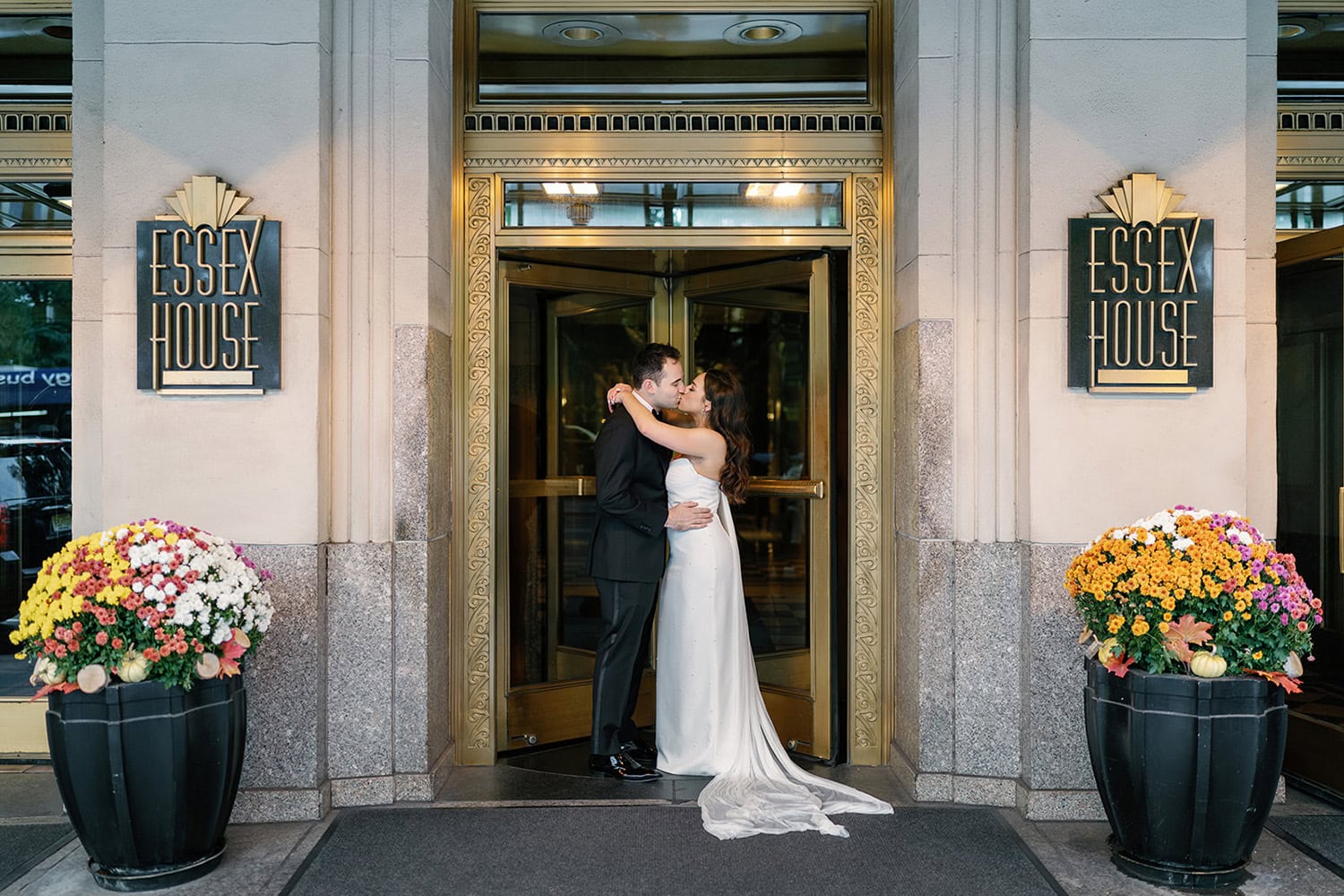 Bride and groom share a kiss at the entrance of JW Marriott Essex House, framed by the hotel’s iconic Art Deco signage and floral arrangements.