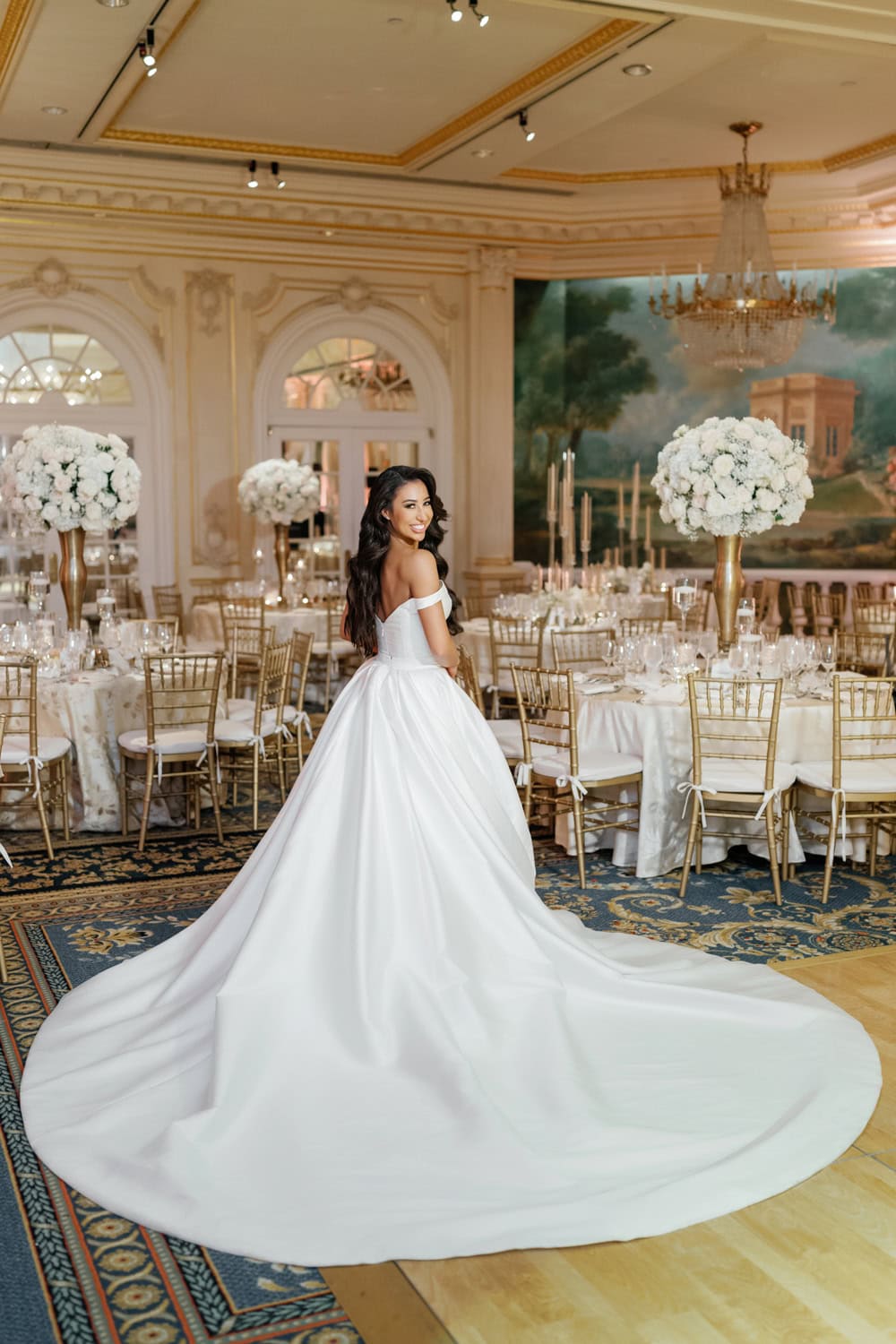 Bride in an elegant white gown posing inside the Grand Salon at JW Marriott Essex House, surrounded by luxurious floral decor and chandeliers.