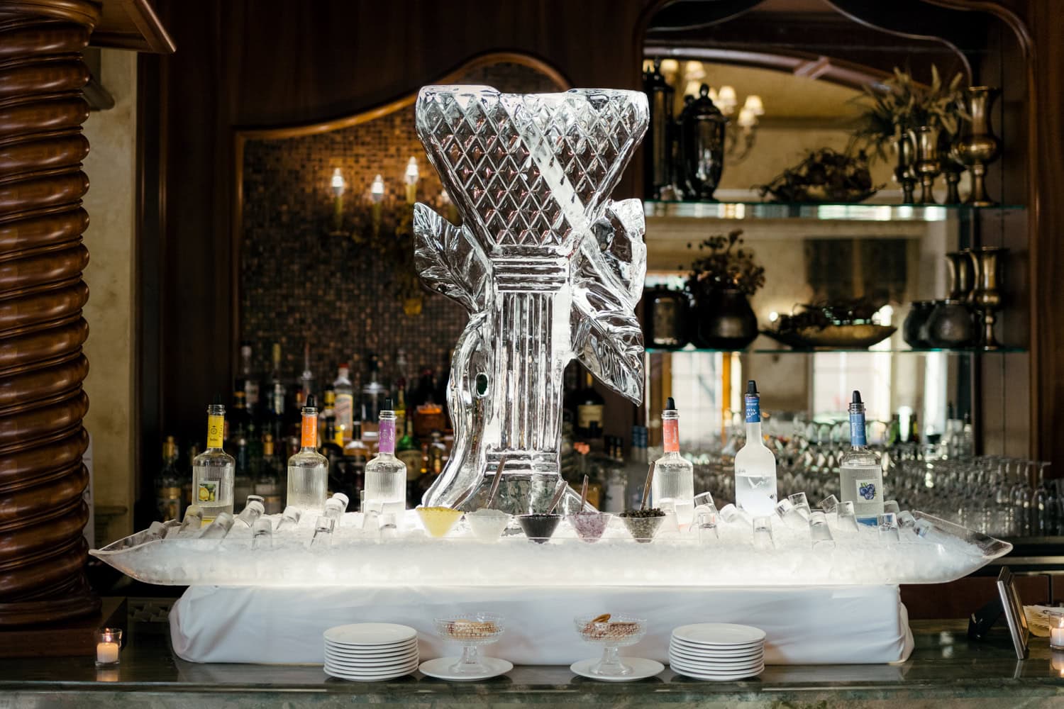 An extravagant cocktail hour display at The Venetian, featuring an elegant ice sculpture, premium vodka bottles, and gourmet garnishes on a bed of ice.