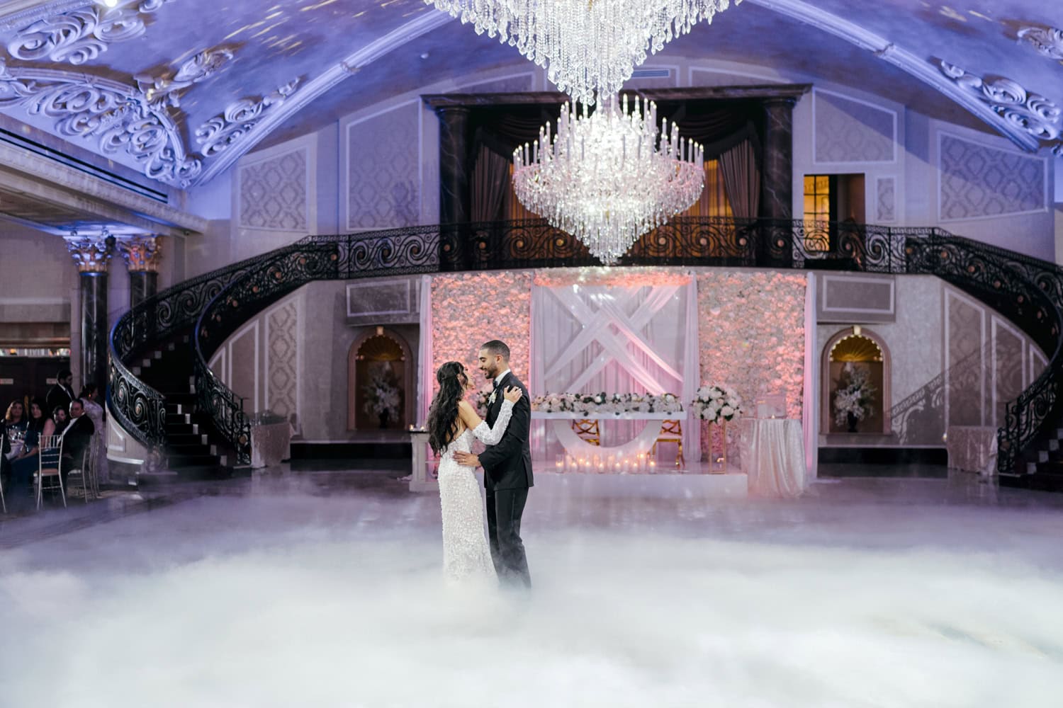 Bride and groom share a romantic first dance, surrounded by a dreamy fog effect under grand chandeliers in the elegant Palazzo ballroom.