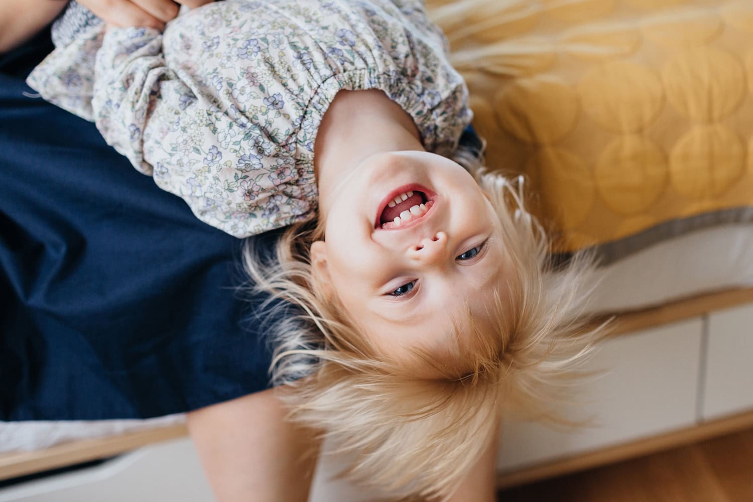 A laughing toddler plays upside down during a fun and relaxed at-home family photography session.