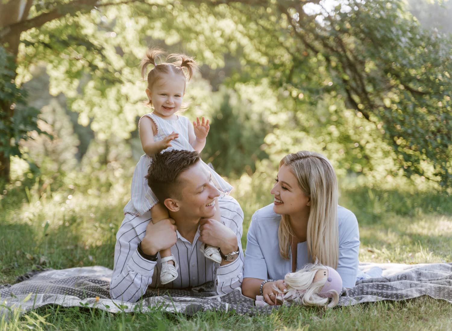 A little girl sits on her dad’s shoulders while her parents laugh together during a relaxed family photoshoot in Armonk, NY