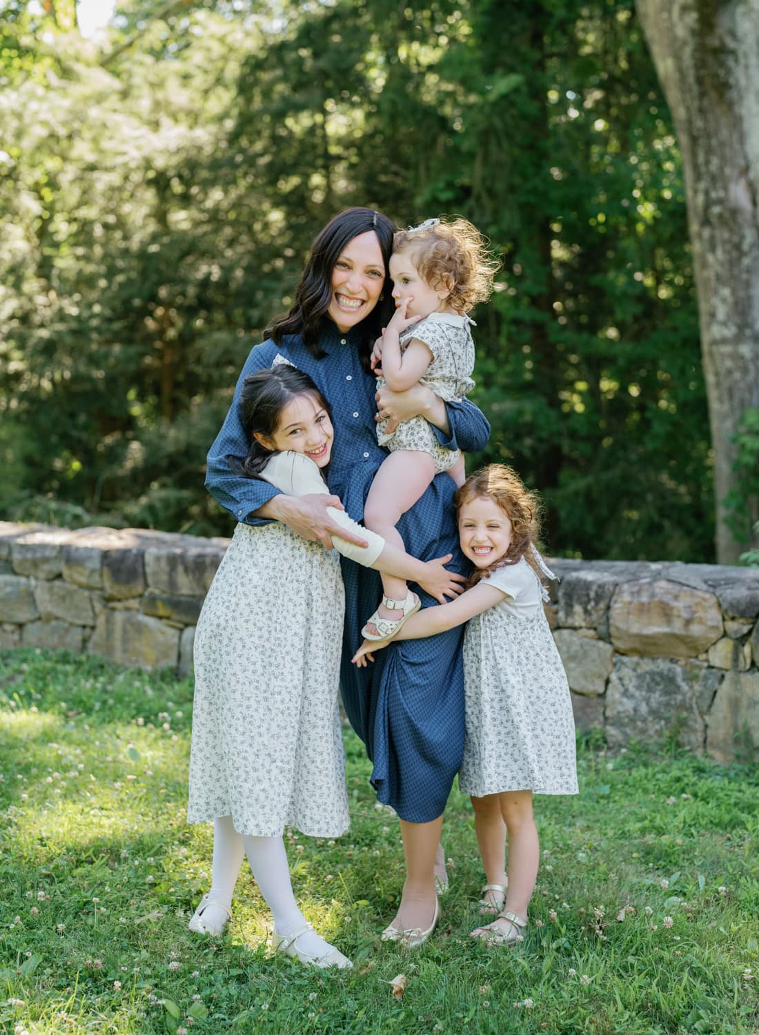Mother embracing her three daughters in a warm outdoor family portrait session in Larchmont, NY.